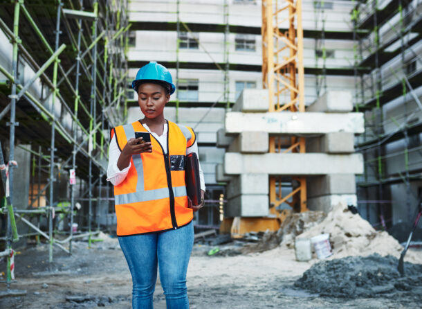Photograph of a woman holding a cell phone in front of a construction site